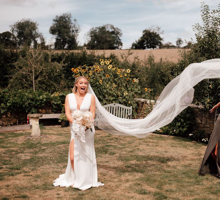 Bride wearing a satin wedding dress with deep plunge and cathedral length veil with a bridesmaid in a brown satin dress 