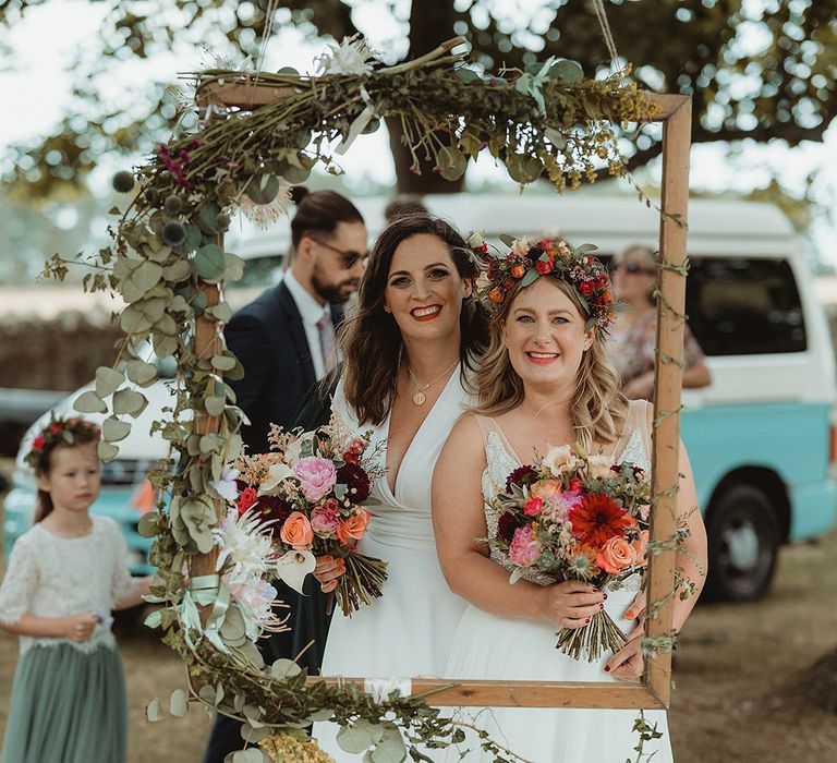 Two brides smile together through hanging wooden frame photo decoration 