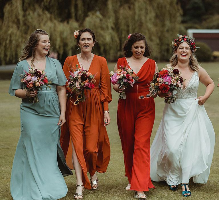 Bridesmaids in mismatched bridesmaid dresses in different colours and styles with matching sunglasses and colourful wedding flowers 