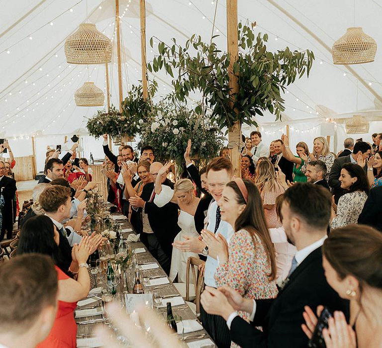 Wedding guests celebrate in marquee complete with hanging floral installations 