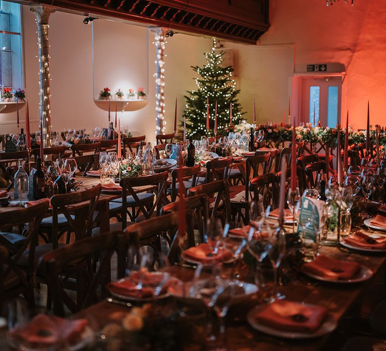 Reception room of Marylebone Town Hall with silver and gold wedding streamers, orange tapered candles, orange napkins, orange rose and foliage tablerunners, fairy lights and large Christmas tree 