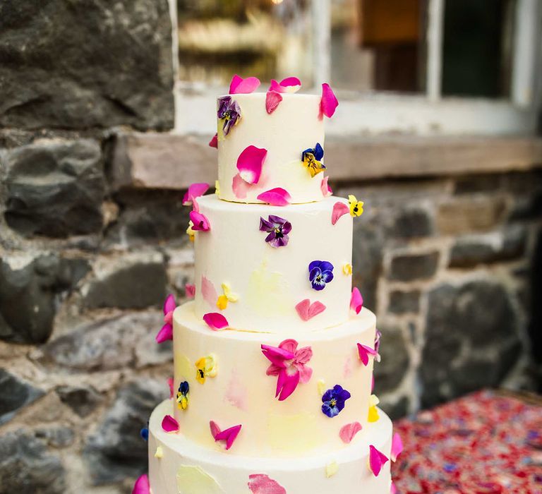 White frosted four tier wedding cake complete with colourful pressed petals 