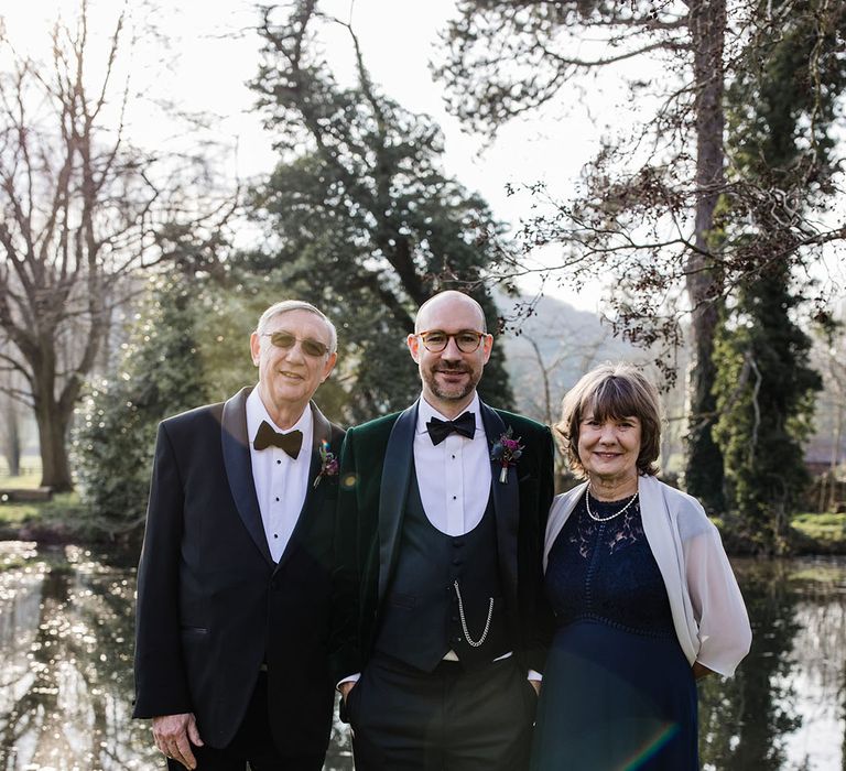 Groom wearing a green velvet tuxedo smiling with his parents on the wedding day