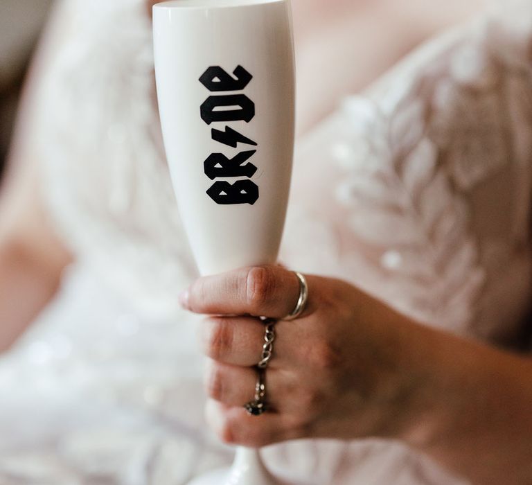 Bride in 3d appliqué wedding dress holding white personalised champagne glass with "bride" in black lettering and AC/DC font and lightning bolt 