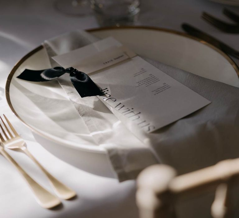 Minimalistic monochrome wedding stationery with black ribbon on elegant ceramic plate with golden cutlery 