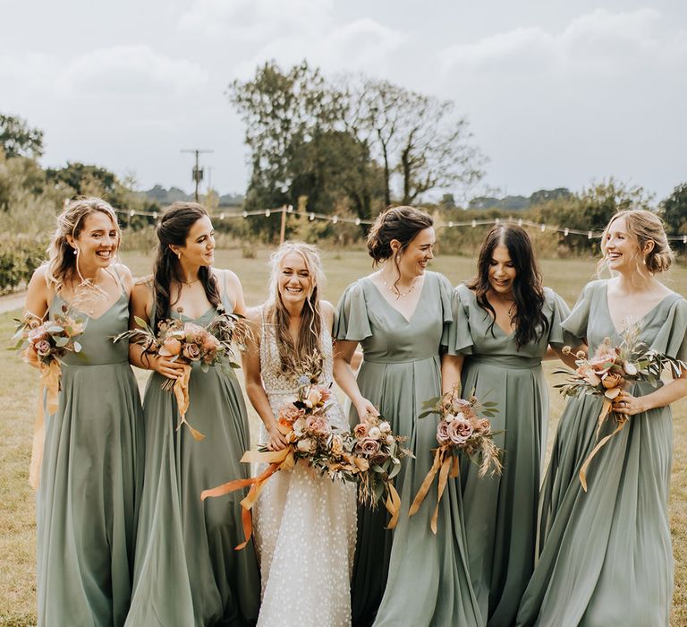 Bridesmaids in thin strap and short sleeve green bridesmaid dresses from TH&TH bridesmaids with the bride in a patterned Made With Love wedding dress 