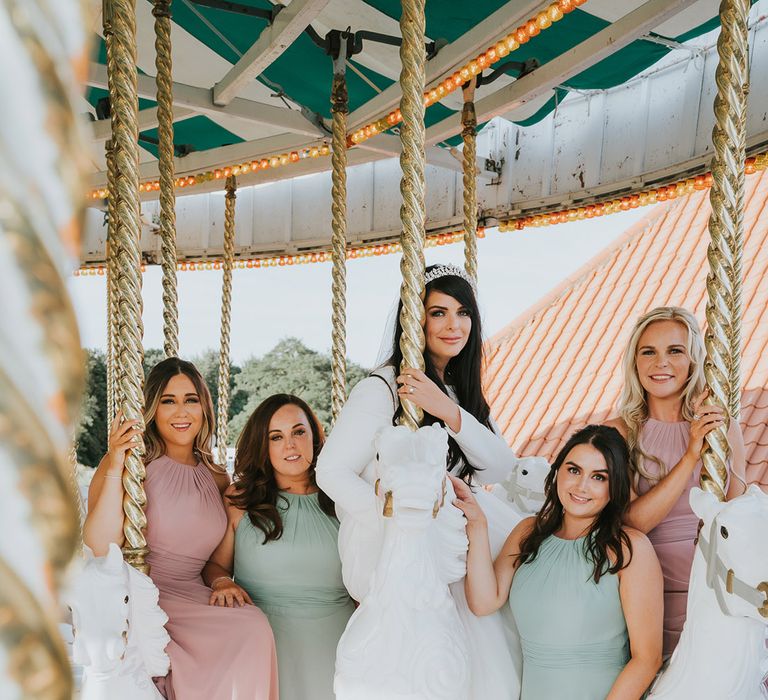 Pastel pink and green wedding theme with the bridesmaids in matching pink and green bridesmaid dresses with the bride in a high neck long sleeve wedding dress on the carousel