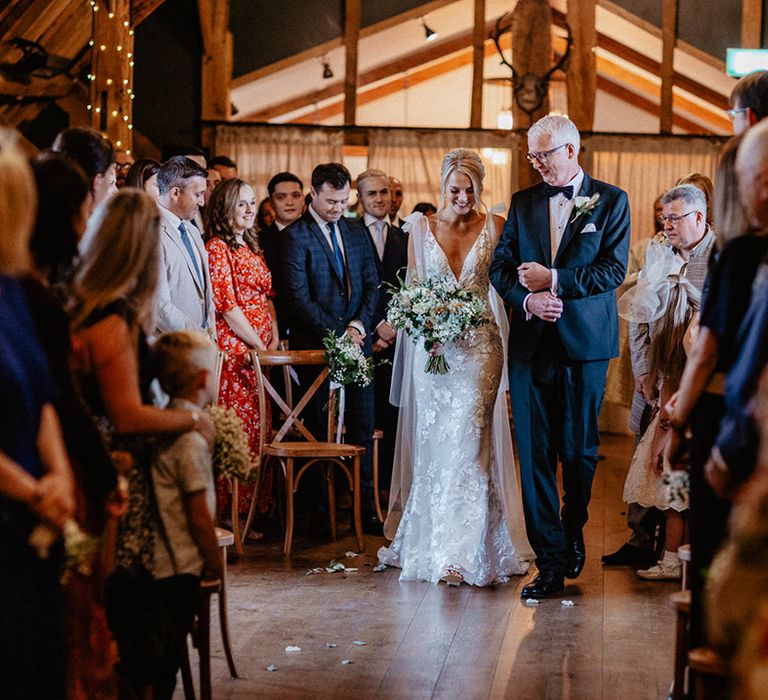 Father of the bride in black tie walks the bride in a fitted lace wedding dress down the aisle at Silchester Farm wedding 