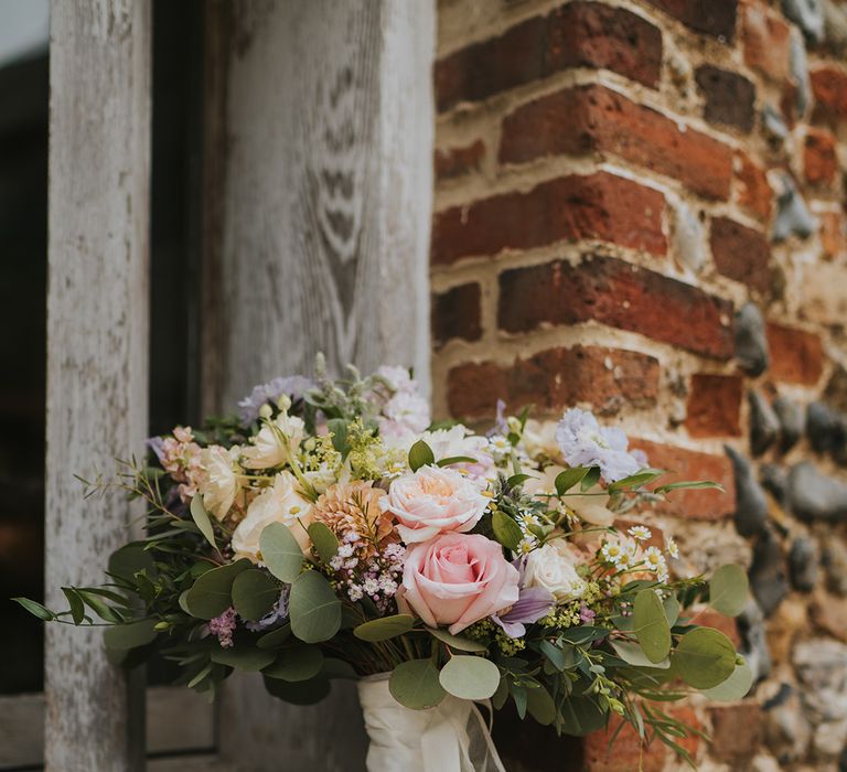 Bride's pink rose, daisy, purple and orange flower bouquet with foliage tied with white ribbon 