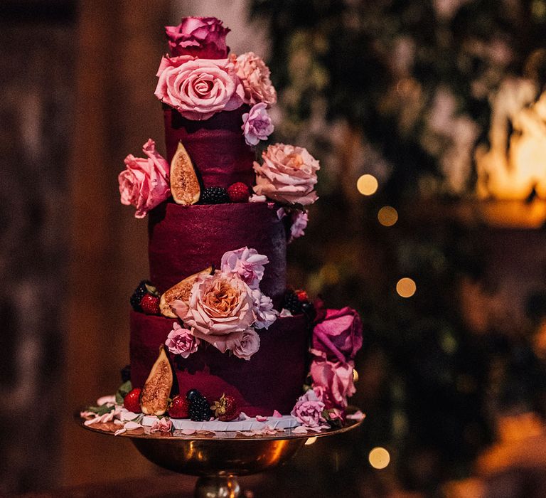 Dark red wedding cake with three tiers decorated with fresh summer berries and pink flowers 