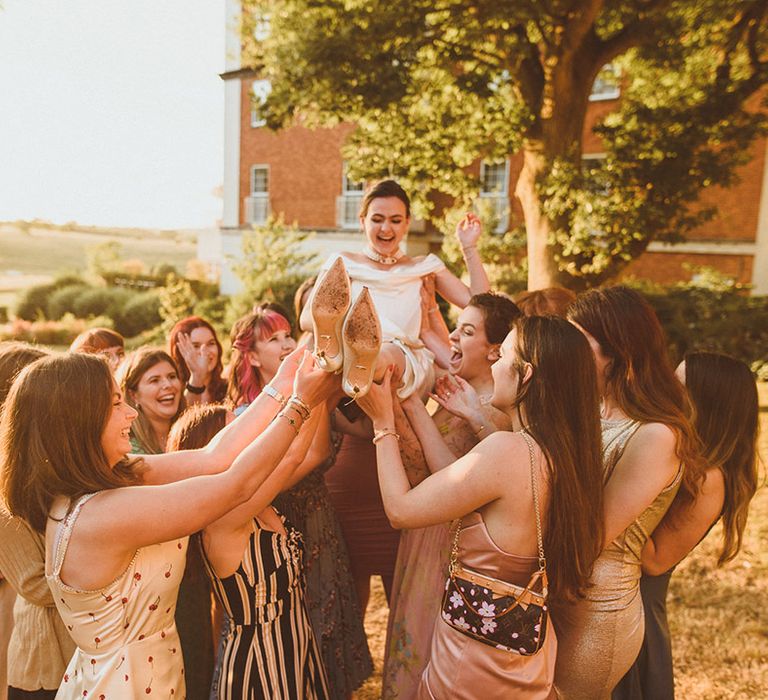 The bridal party and female guests lift up the bride to celebrate the wedding 