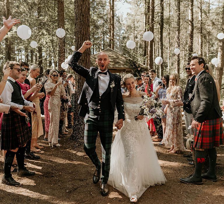 White paper wedding lanterns decorating the outdoor ceremony area with the bride in a floral wedding dress and groom in bespoke checkered wedding trousers