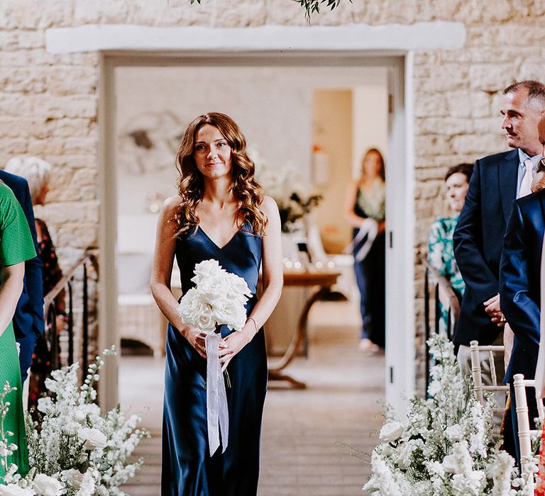 The bride's best friend wearing a navy bridesmaid dress holding white wedding bouquet 