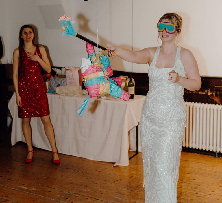 Bride in square neck sequin sparkly reception dress whacking the wedding piñata 