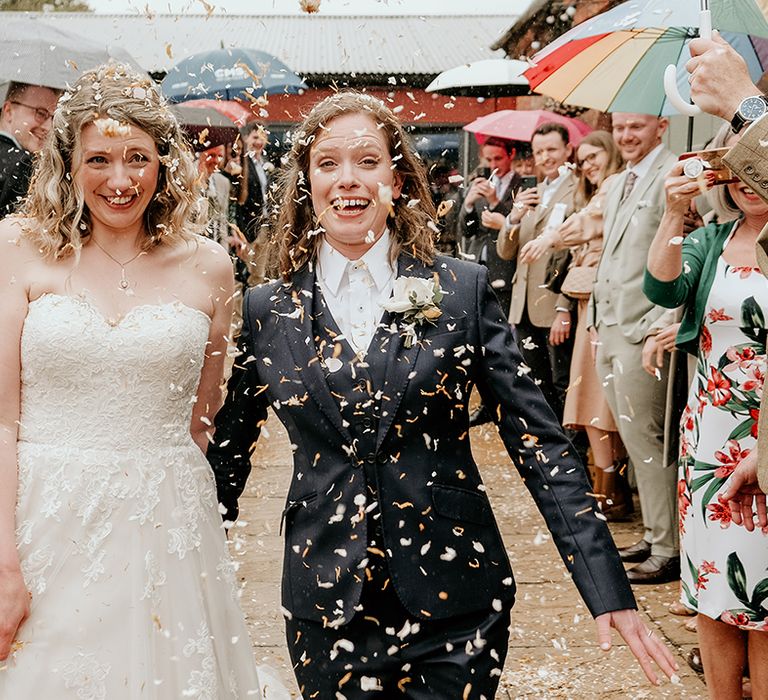 confetti moment with two brides in a strapless lace dress and navy suit at Shropshire wedding venue 