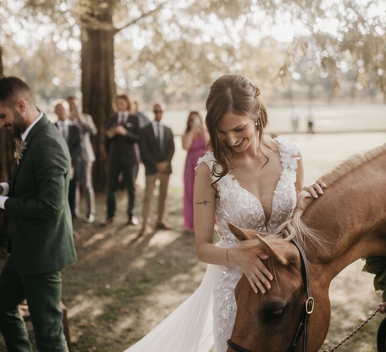 bride in an appliqué wedding dress with her horse wearing a flower collar as the ring bearer 