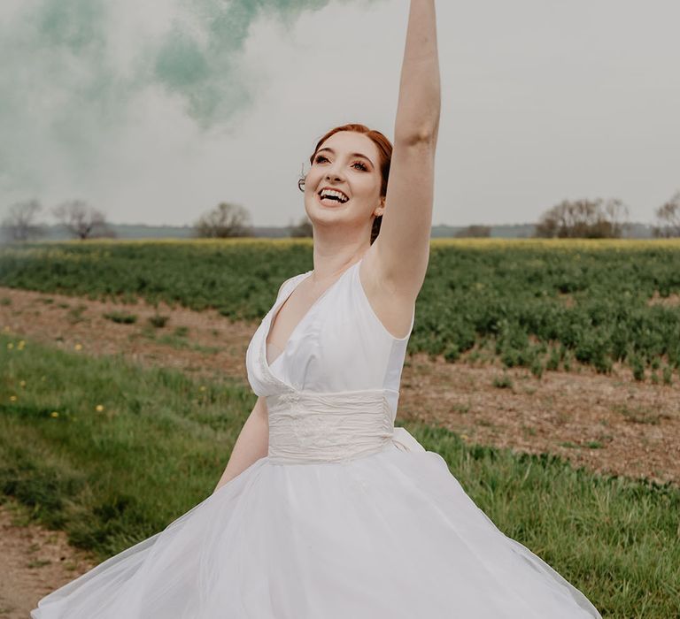 Bride in fitted wedding dress waving green smoke bomb at fun festival wedding 