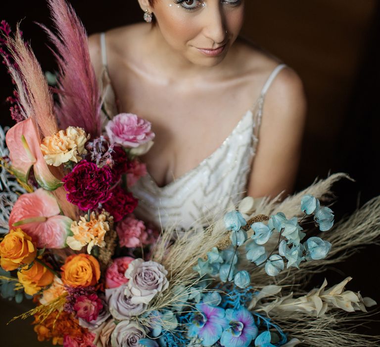 Bride with short hair wearing embellished hair accessories holding a colourful dried flower bouquet 