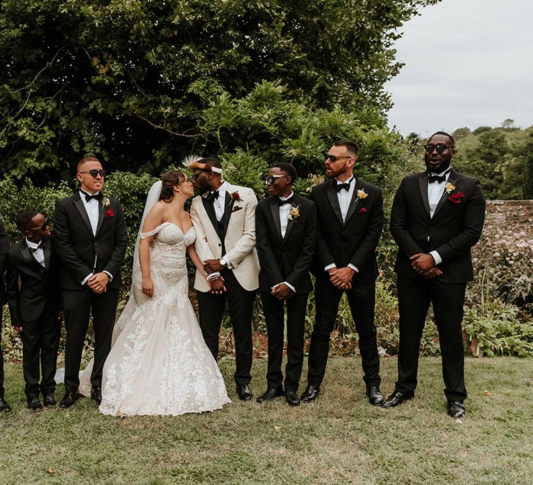 Groomsmen in black tuxedos with the bride and groom sharing a kiss 