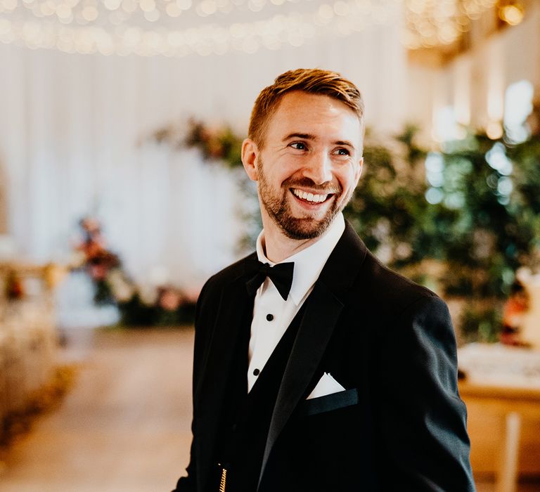 Groom in black tuxedo with gold pocket watch smiling 