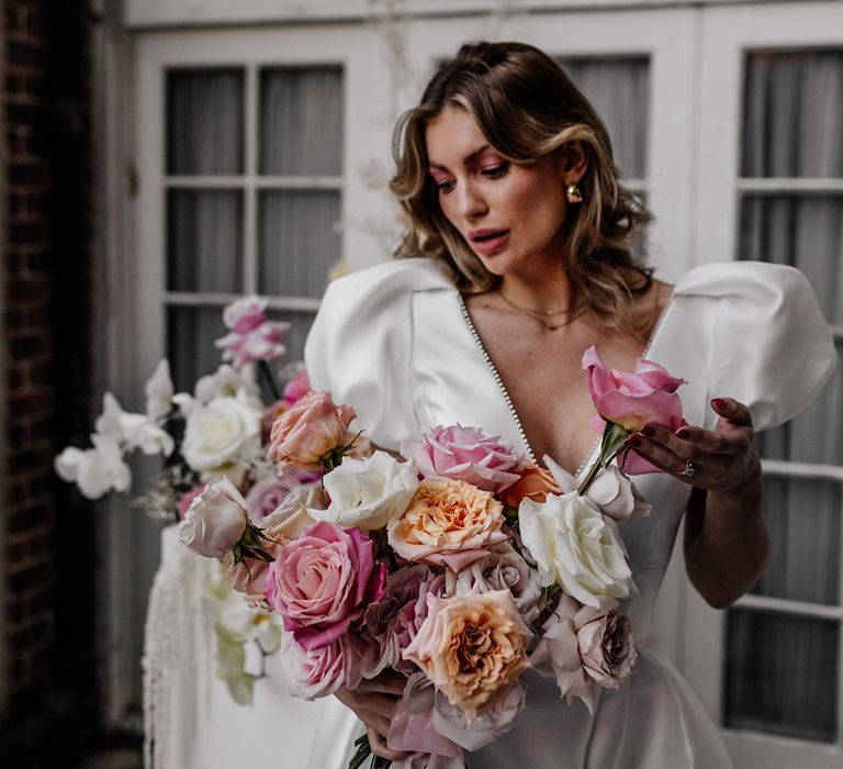 Bride in statement puff sleeve wedding dress holding different coloured bouquet of roses 