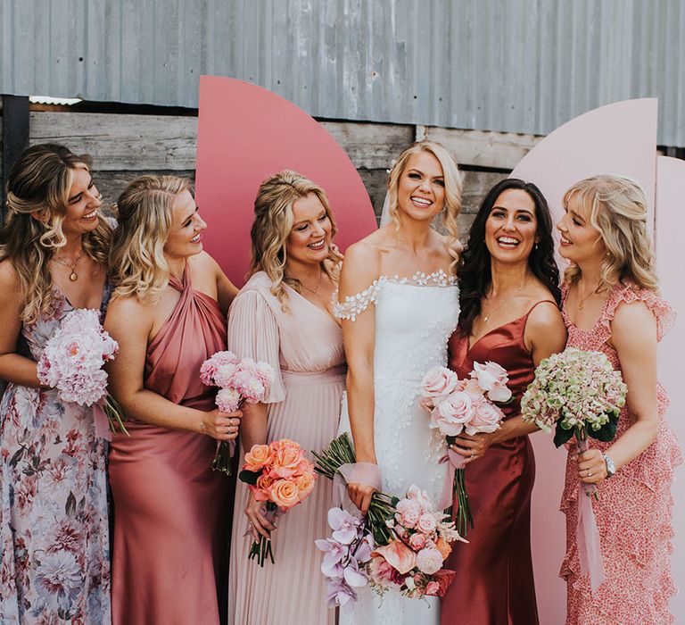 Bridal party wearing mismatched bridesmaid dresses in different patterns and shades of pink 