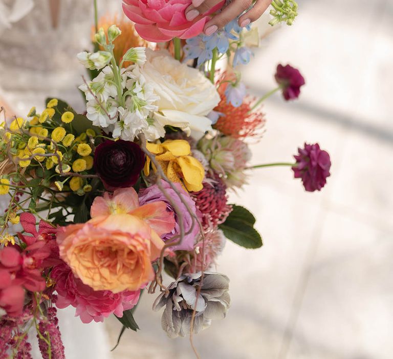 The bride holds a colourful wedding bouquet with blue, pink and yellow flowers 