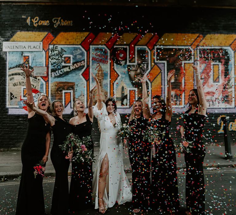 Colourful confetti moment with the bridesmaids wearing black bridesmaid dresses with the bride in front slit wedding dress 