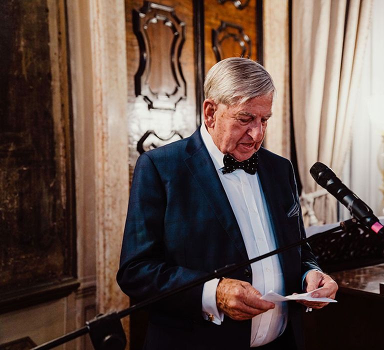 Father of the groom wearing blue suit reading wedding speech 