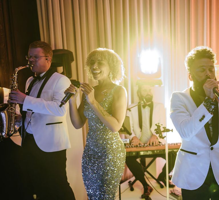 Wedding band plays at wedding reception in white tuxedos with silver sparkly dresses 