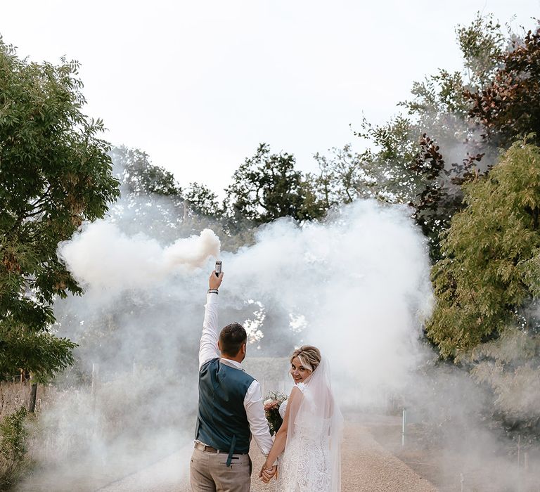 Groom waving grey smoke bomb as he poses with the bride for their couple portrait 