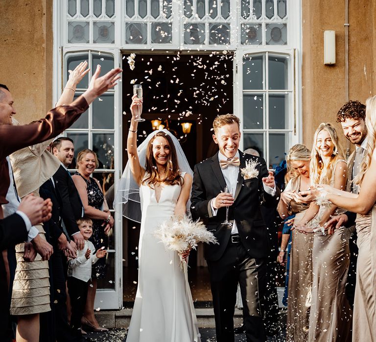 The bride in a plunging wedding dress exits from the wedding ceremony with the groom as the guests throw confetti 