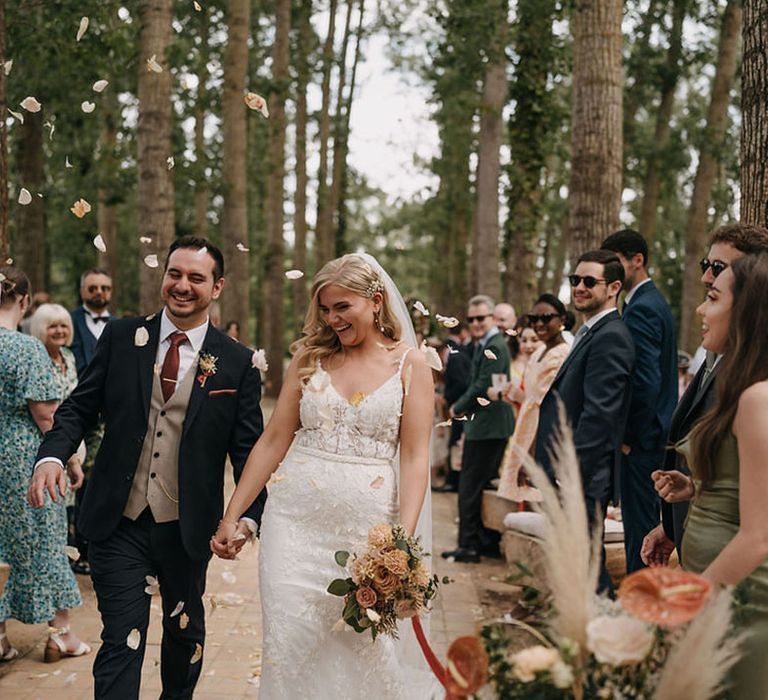 Groom in three piece wedding suit walking out of the ceremony with the bride to confetti 