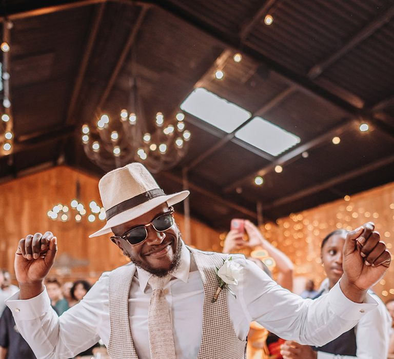 Groomsman wearing beige waistcoat over white long sleeve shirt with wedding hat dancing at reception 