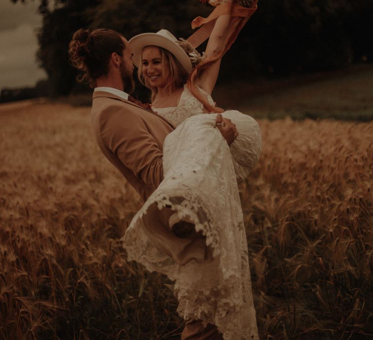 Groom picking his bride up in a corn field