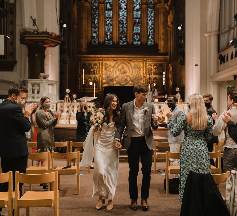 Bride and groom descending up the aisle after their socially distance Holy Trinity Brompton Church wedding ceremony 