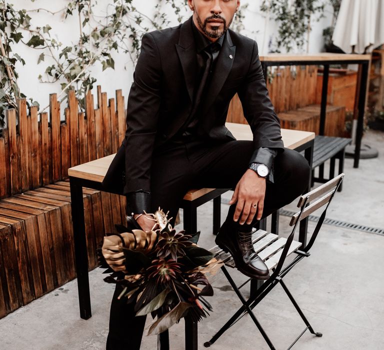 Groom in black suit holding bouquet 