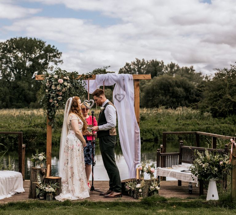 Bride and groom under wooden archway with floral decoration 