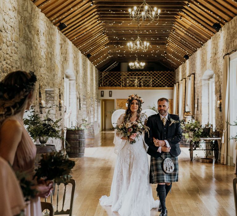 Emotional boho bride with pink rose flower crown and white rose bouquet walks down the aisle with father