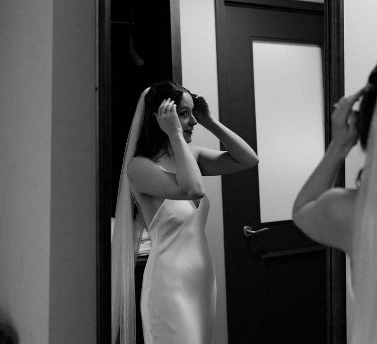 Bride fixing her hair wearing simple wedding dress and veil for London elopement 