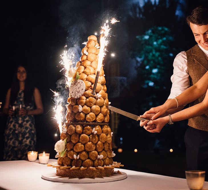 Couple slicing through croquembouche together with flare sparklers on either side