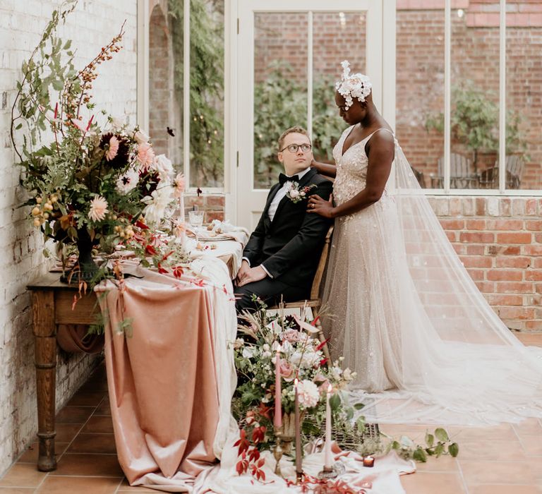 Bride with alopecia standing next to her groom at their intimate reception in a blush pink Julita Bridal London wedding dress with watteau train 