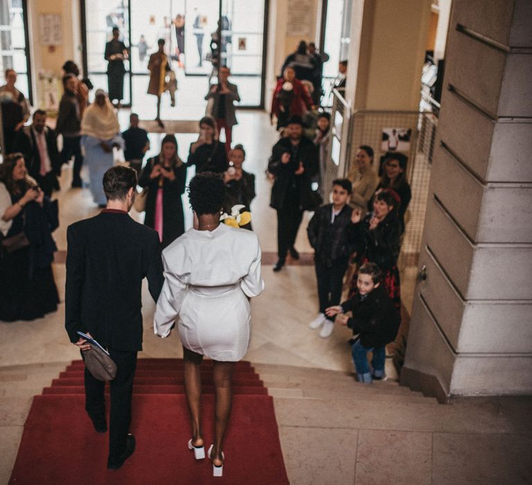 Bride in a short wedding dress and mules walking down the town hall steps with her groom in a black suit 