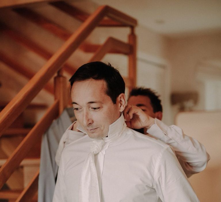 The groom getting ready in a white shirt and white tie