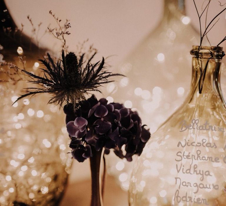 Table seating plan on glass vases lit up by pretty fairy lights