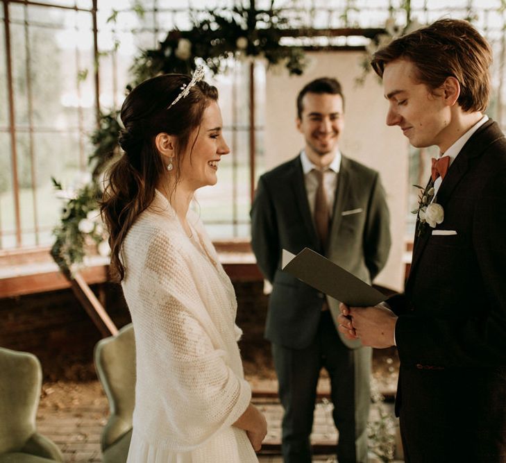 Groom in a black suit with orange bow tie reading his wedding vows 