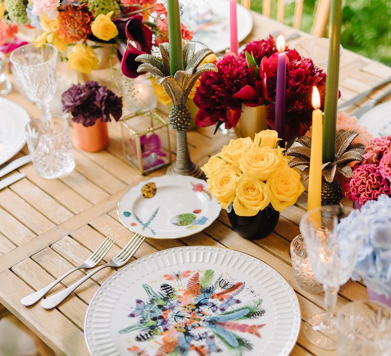 Table setting with bold bouquets lining the table, white plates with colourful printing placed on wooden table