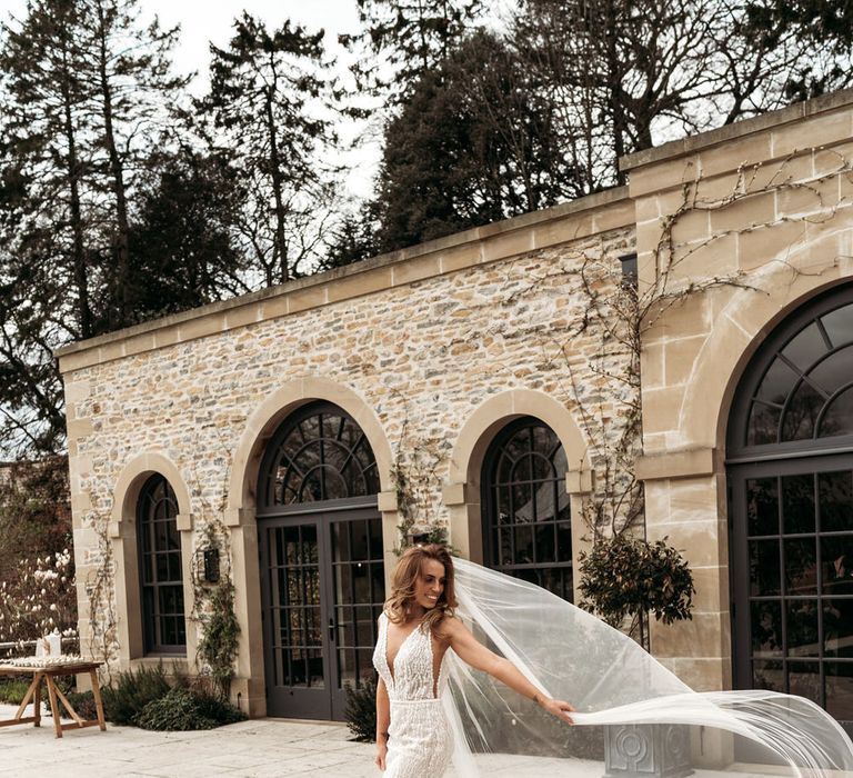 Bride in a fitted wedding dress with plunging neckline and sheer side panel wearing a long veil 