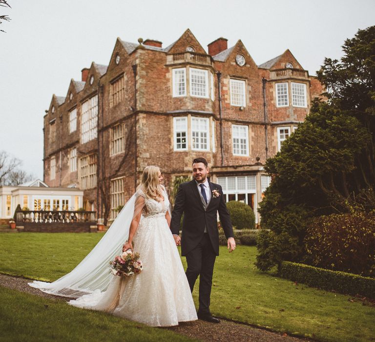 Bride in a princess wedding dress and groom in navy suit walking through the grounds at Goldsborough Hall 