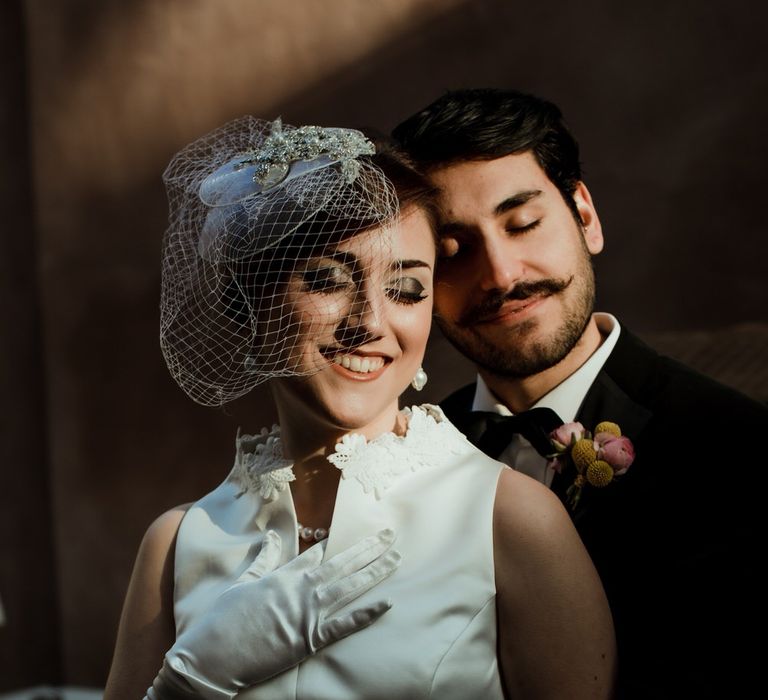 The bride and groom posing in the sunlight with their eyes closed for their vintage themed wedding